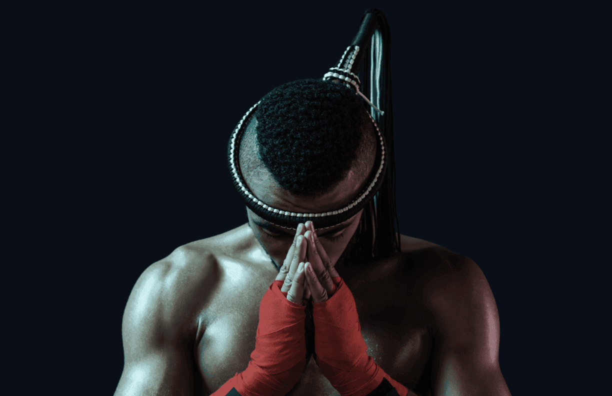 Athlete in a mongkol and red hand wraps, head bowed before training