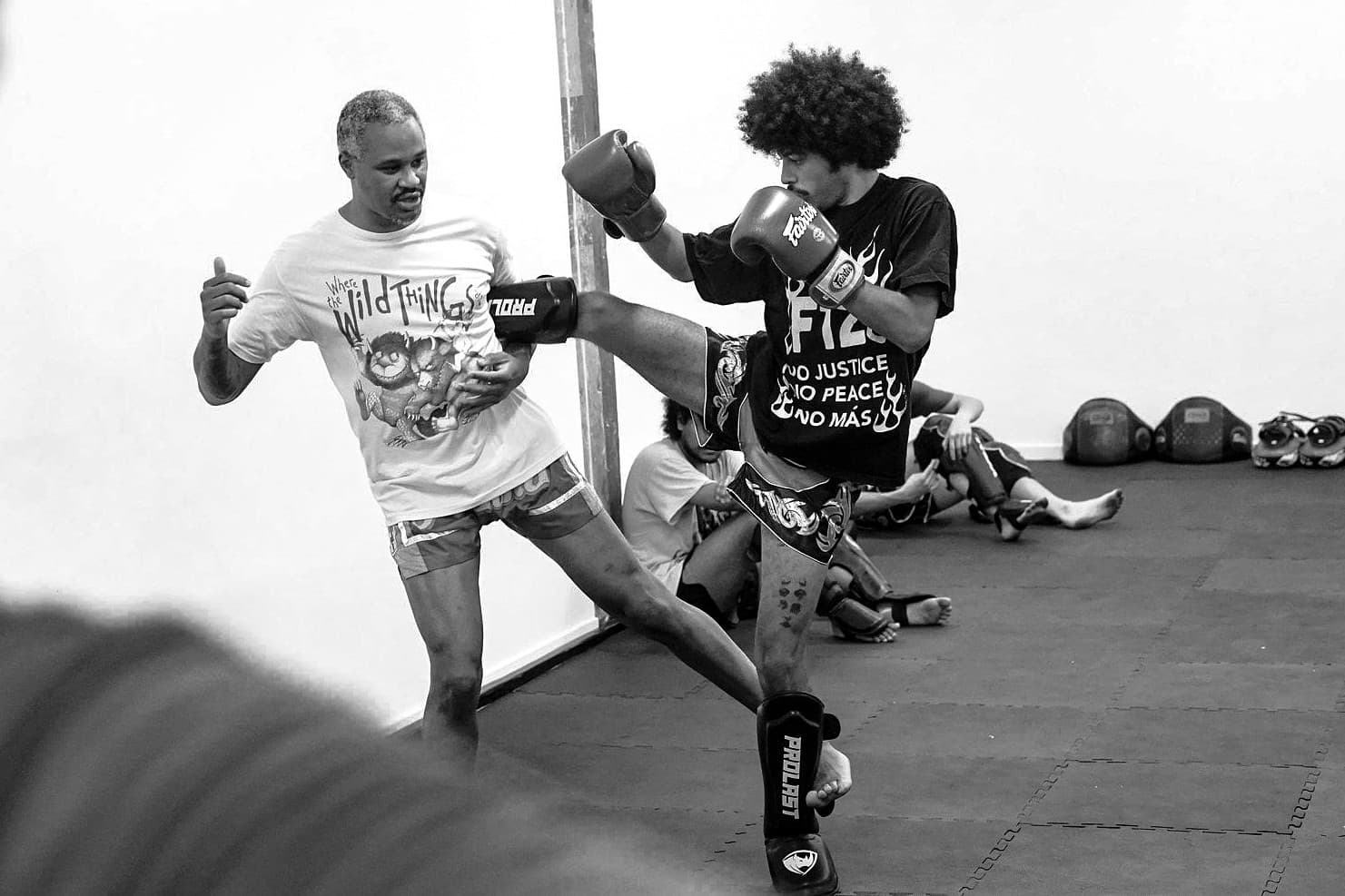 Coach Al catching a student's high kick mid-instruction on the mats