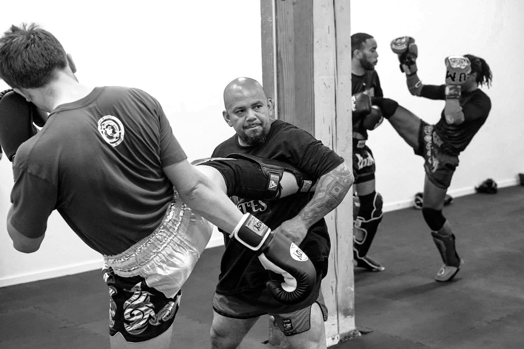 Coach Cortes catching a student's kick on shin pads during class