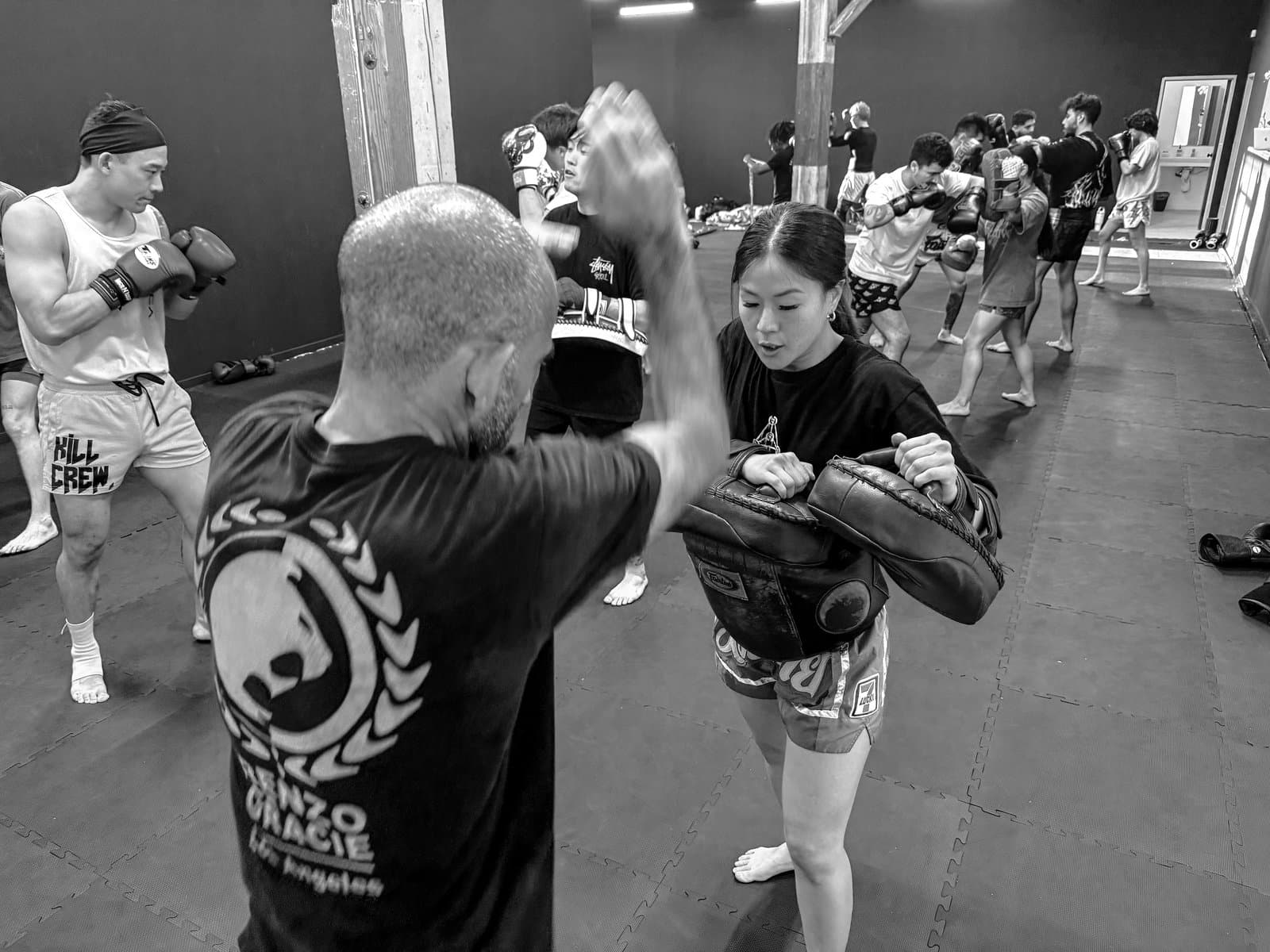 Coach Phoebe holding Thai pads for a student in a packed class